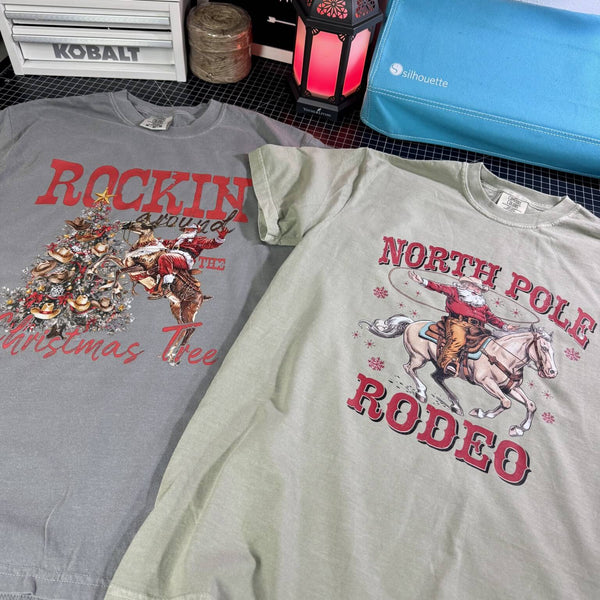 Two t-shirts with Cowboy Santa Christmas-themed designs on a surface.