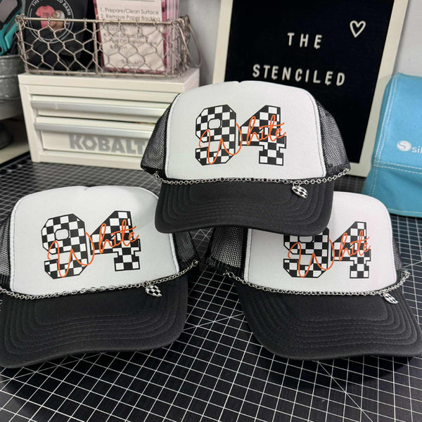 Three trucker hats with checkered patterns and numbers on a grid surface.