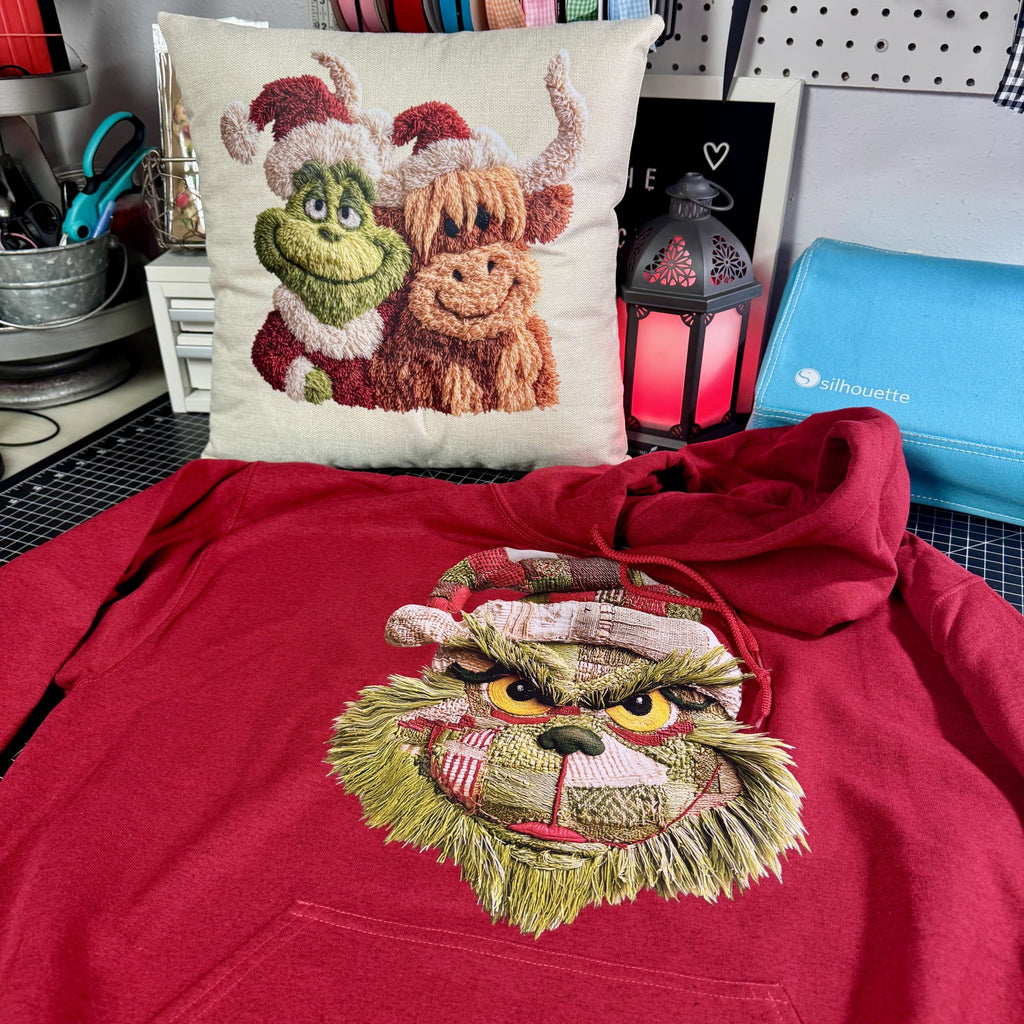 Red hoodie with faux embroidered design of a character wearing a Santa hat, next to a pillow with similar design.