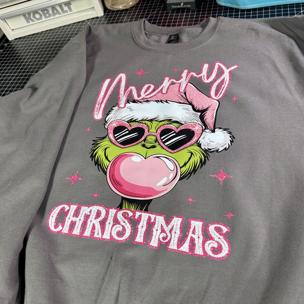 Gray sweatshirt with a festive design featuring a character wearing a Santa hat, sunglasses, and a heart-shaped bubble gum. The text 'Merry Christmas' is displayed.