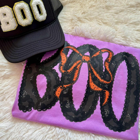 Black cap with 'BOO' text and purple shirt with 'BOO' and bow design on a fluffy white surface