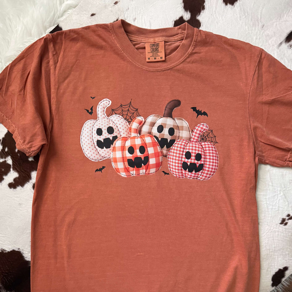 Orange t-shirt with Halloween-themed pumpkins design on a cowhide rug background