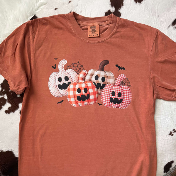 Orange t-shirt with Halloween-themed pumpkins design on a cowhide rug background