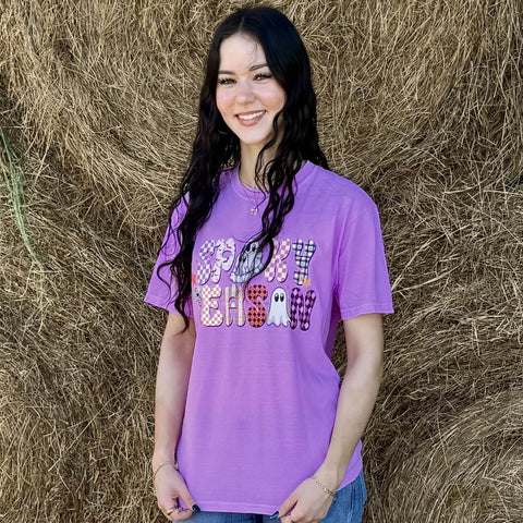Woman wearing a purple 'Spooky Season' shirt standing in front of hay bales.