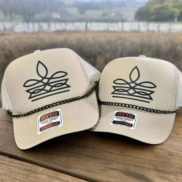 Two beige caps with black boot stitch design and Otto trucker hat label on a checkered surface.