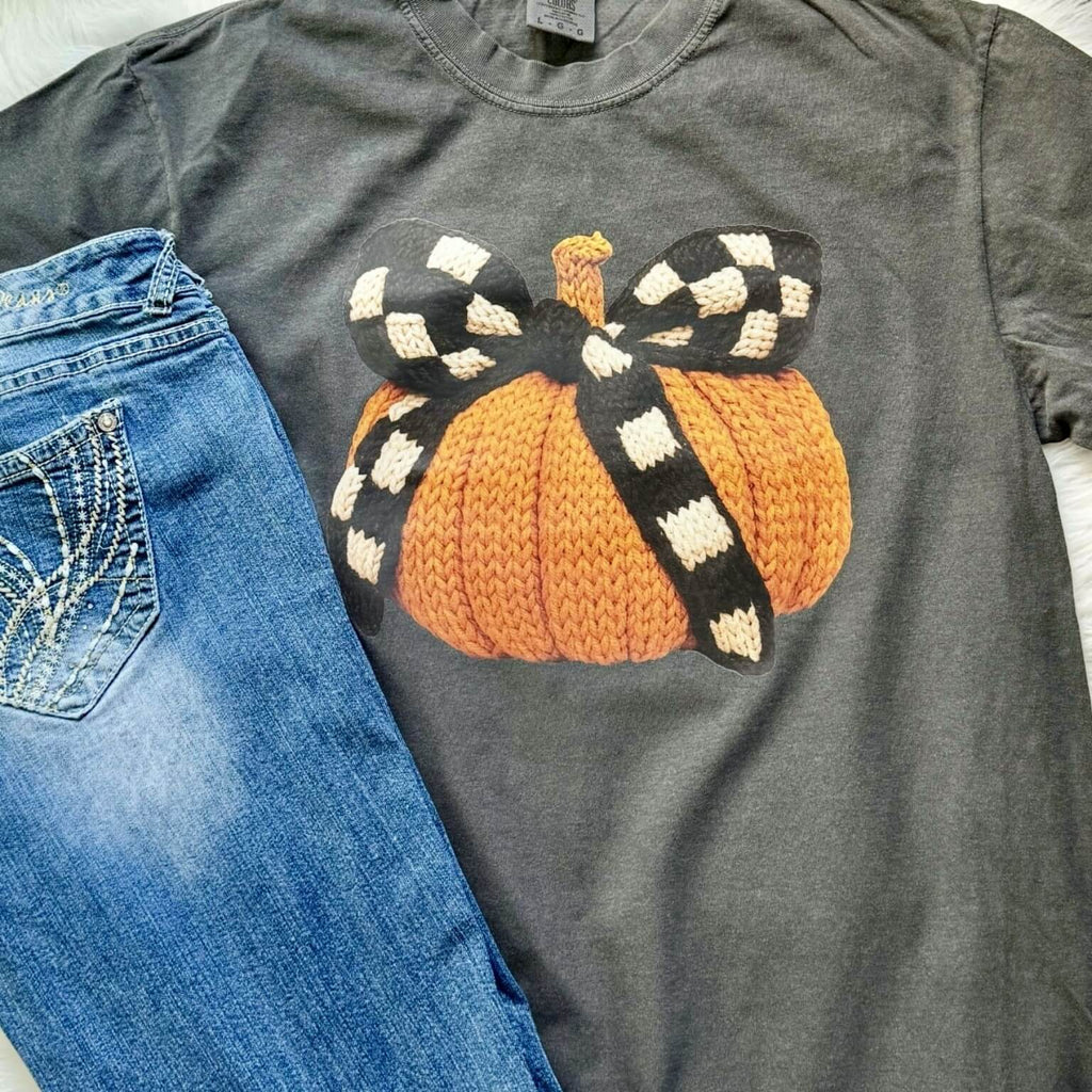 Gray t-shirt with a knitted pumpkin and checkered bow design next to blue jeans