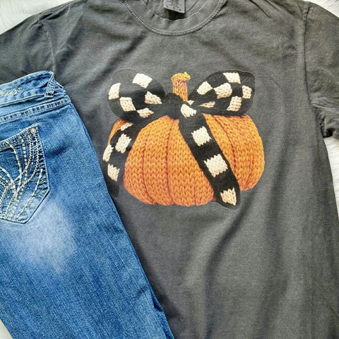 Gray t-shirt with a knitted pumpkin and checkered bow design next to blue jeans
