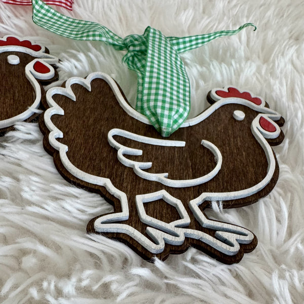 Close-up of 3D wooden chicken ornament with dark rustic wood grain, raised white outline, red accents and green gingham ribbon.
