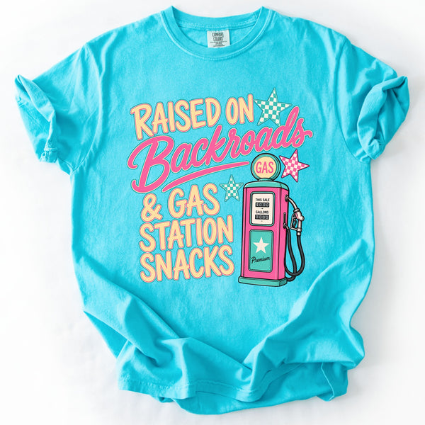 Comfort Colors Lagoon Blue graphic tee with retro Raised On Backroads & Gas Station Snacks design featuring pastel lettering and vintage gas pump graphic laid flat on white background