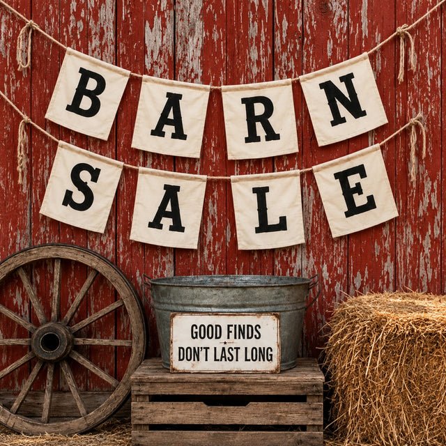 Rustic Barn Sale collection display with canvas letter banners on a weathered red barn wall, vintage wagon wheel, hay bale, and galvanized tub with Good Finds Don't Last Long sign.