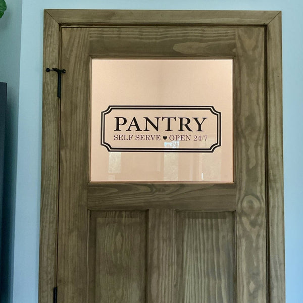 Rustic wood pantry door with glass window featuring black Pantry Self Serve Open 24/7 vinyl door decal.