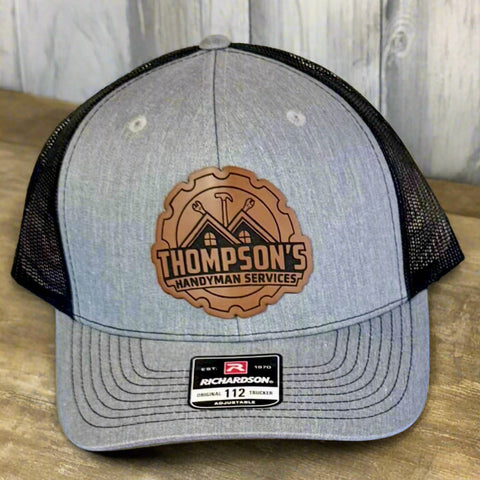 Men's Richardson 112 Trucker Hat with Engraved Business Logo Leather Patch sitting on a wooden table