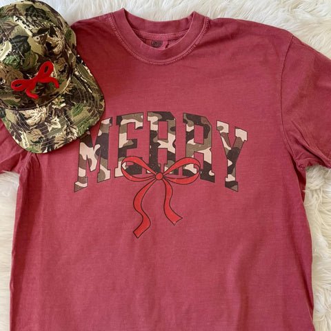 Vintage red Christmas tee with the word “Merry” in camo letters and a red bow, styled with a camo hat.