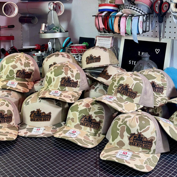 Camo trucker hats with custom leather patches in tan brown and green outdoor style