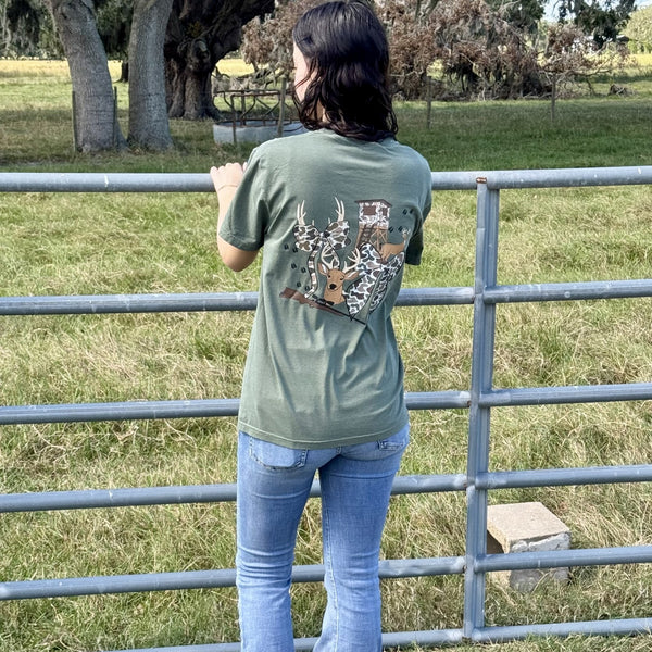 Person wearing a green t-shirt with a deer design, standing by a metal fence in an outdoor setting.