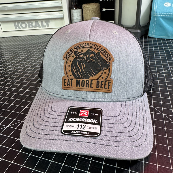 Gray and black Richardson 112 trucker hat with brown leather Eat More Beef patch featuring a cattle rancher design.