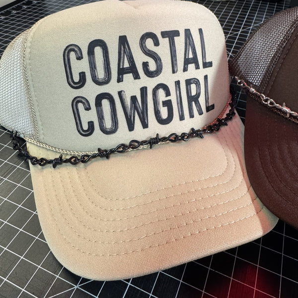 Beige cap with 'Coastal Cowgirl' text and chain detail on a grid background