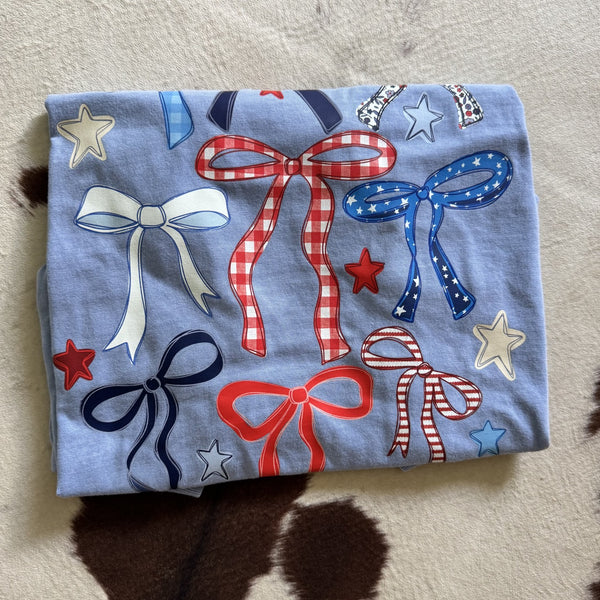 Patriotic coquette bows graphic tee featuring red white and blue ribbon bows and stars on light blue shirt