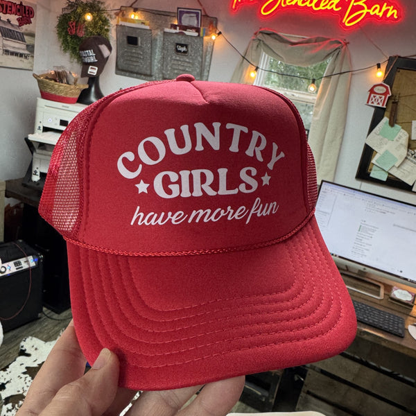 Red cap with 'Country Girls have more fun' text held in front of a computer desk.