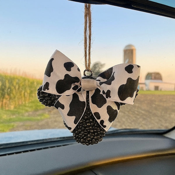 Car air freshener with cow print bow and black beads hanging from a car's rearview mirror.