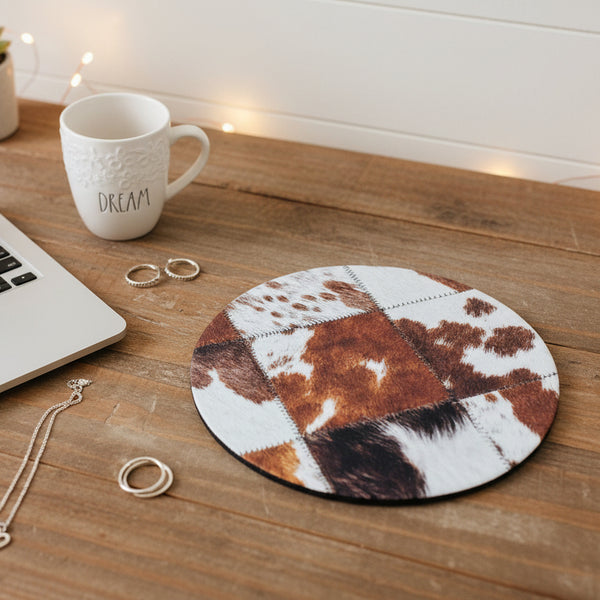 Round cowhide rug on a wooden surface with a mug, laptop, and jewelry.
