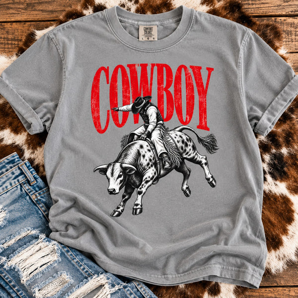 Gray Comfort Colors retro rodeo graphic tee with cowboy riding a bucking bull, styled with distressed denim, cowhide, and rustic wood background.