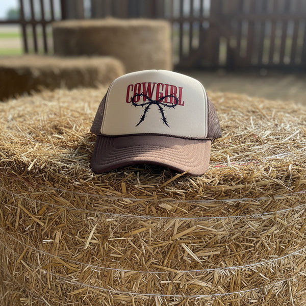 Trucker hat with 'Cowgirl' and barbed-wire design sitting on a roll of hay.