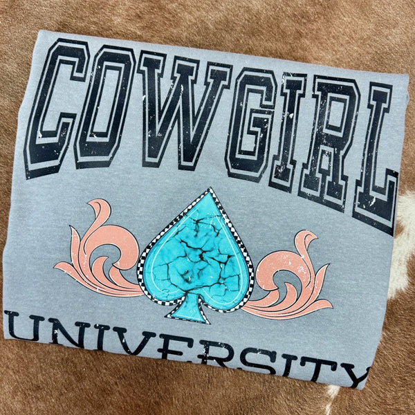 T-shirt with 'Cowgirl University' text and turquoise spade design on a textured surface