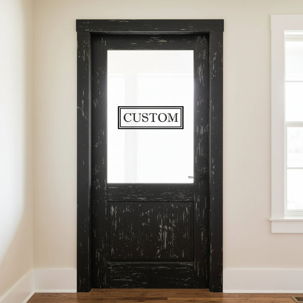 Black wooden door with a 'CUSTOM' vinyl door decal in a room with beige walls and a window.