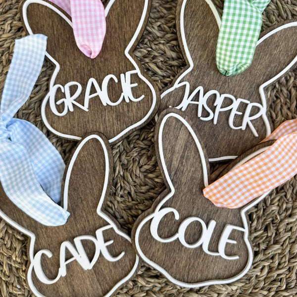 Wooden bunny-shaped name signs with colorful ribbons on a textured surface