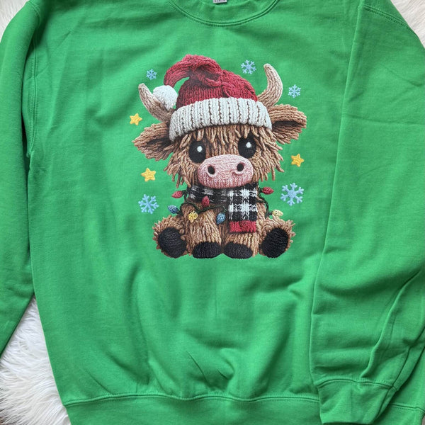 Green sweatshirt with a cartoon Highland cow wearing a Santa hat on a white surface