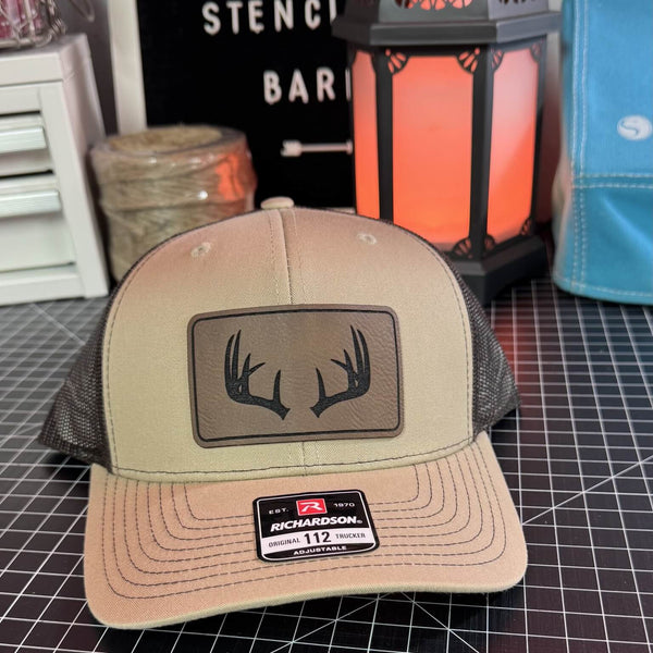 Beige trucker hat with deer antler design on a grid surface