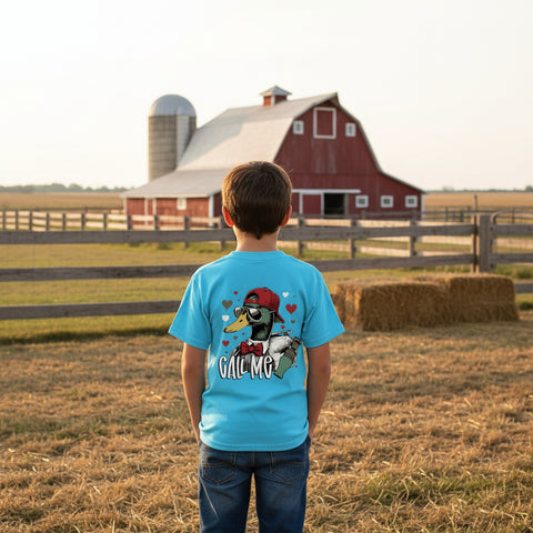 Southern boy wearing a blue Valentine t-shirt with a duck caller design that says Call Me, standing in a field with a barn in the background