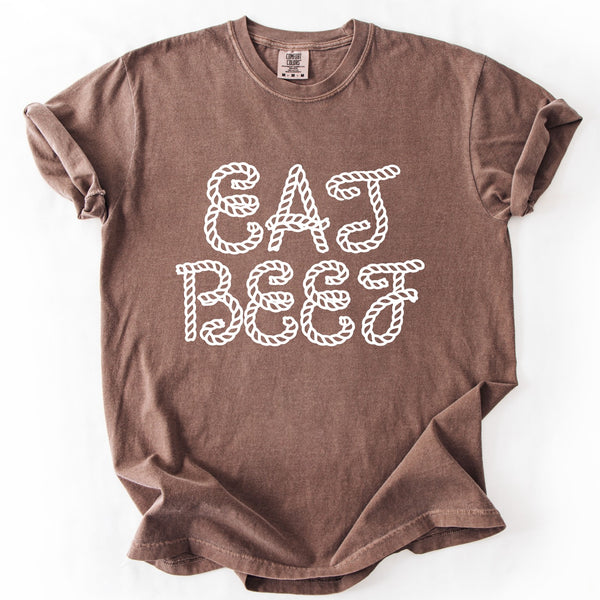 A brown short-sleeve t-shirt with rolled sleeves, featuring the phrase 'EAT BEEF' printed in a white rope-style font on the front, laid flat against a white background.