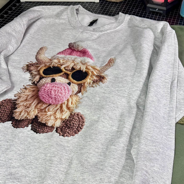Gray sweatshirt with a faux embroidered design of a cow wearing sunglasses and a pink hat.