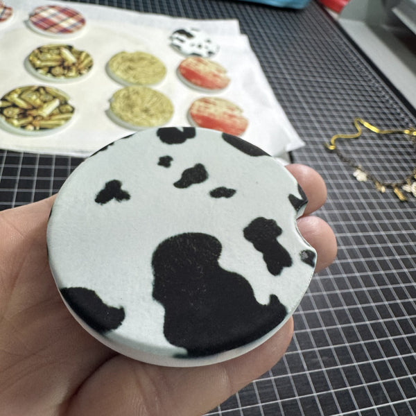 Black and white faux cow print car coaster for vehicle cup holders available in ceramic or neoprene.