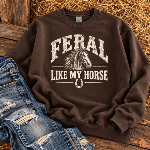 Chocolate brown Feral Like My Horse Gildan crewneck sweatshirt with antique white horse graphic, styled with distressed denim on rustic wood and hay.