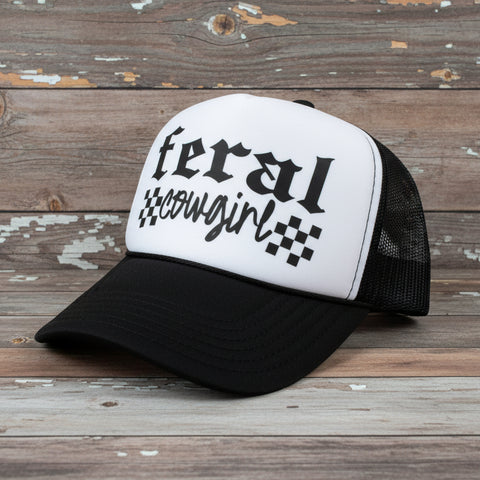 Black and white cap with 'feral cowgirl' text on a rustic wooden background
