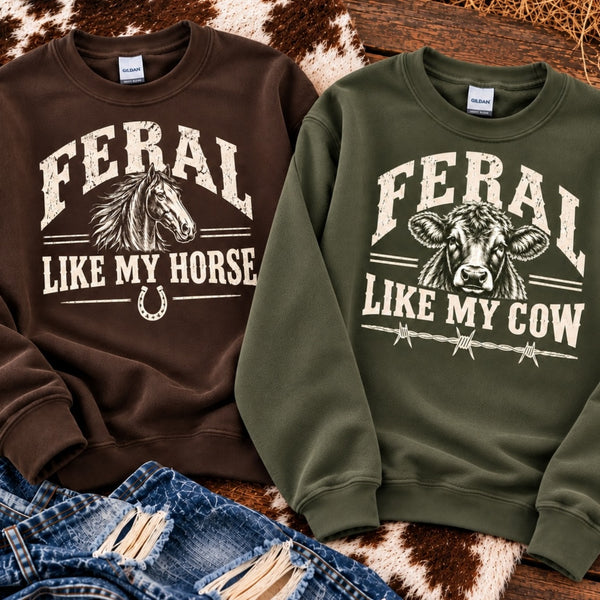 Feral Like My Horse chocolate brown sweatshirt and Feral Like My Cow military green sweatshirt with vintage Western graphics displayed together on rustic wood.