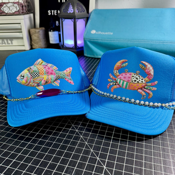 Neon blue mesh trucker hats with colorful patchwork fish and crab graphics featuring trendy coastal summer style and decorative pearl and fishing lure hat chains