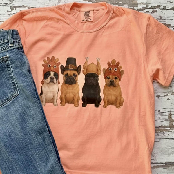 Orange t-shirt with cartoon French Bulldogs wearing Thanksgiving hats on a wooden surface