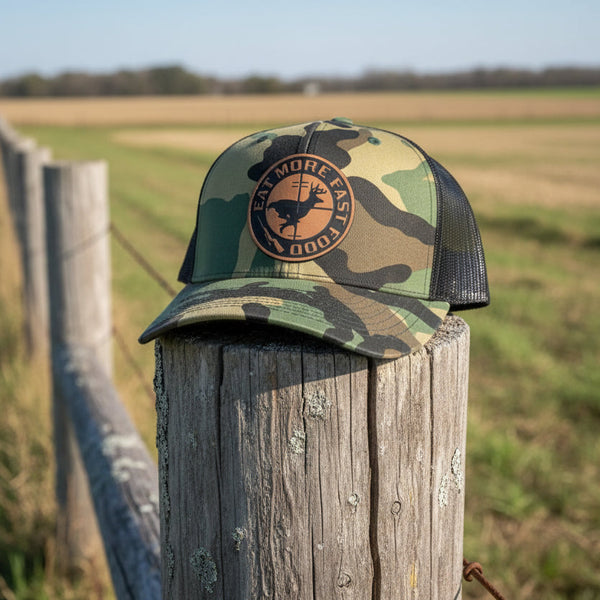 Camouflage cap with a deer hunter design on a wooden post in a field