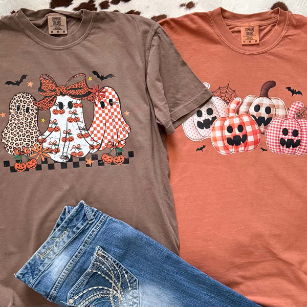 Two Halloween-themed t-shirts with ghosts and pumpkins on a brown and orange background, with a pair of blue jeans in front.