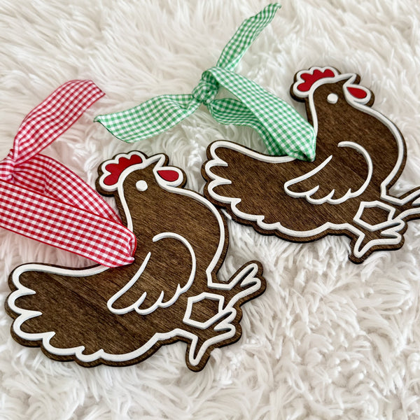 Handmade farmhouse chicken ornaments with layered wood construction and red and green gingham hanging ribbons.