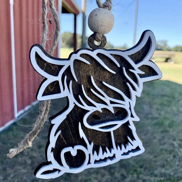 Wooden ornament shaped like a cow with a red barn and green field in the background