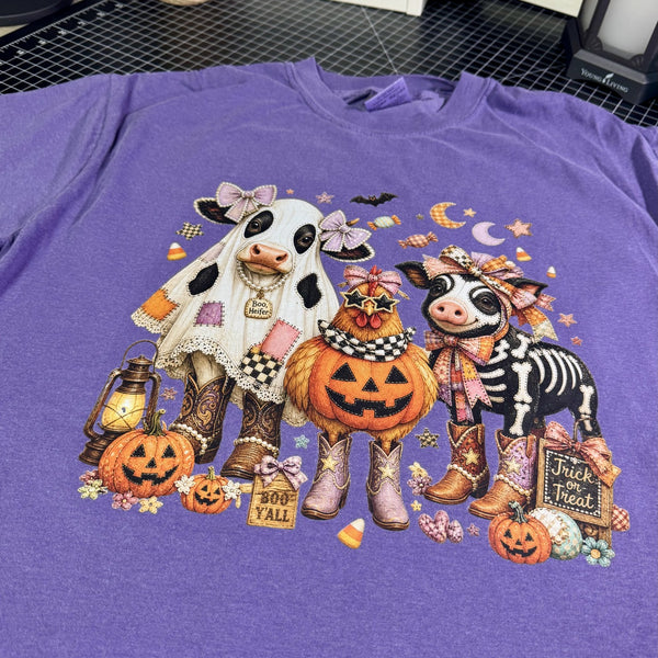 Close-up of Boo Heifer Halloween cow graphic printed on a purple Comfort Colors tee with chicken, skeleton pig, pumpkins and western details