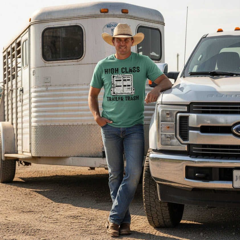 Man wearing green t-shirt with 'High Class Trailer Trash' graphic design standing next to a truck and horse trailer
