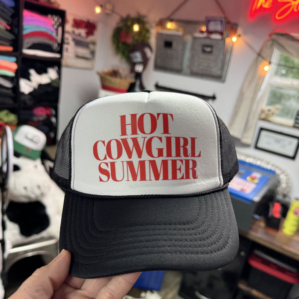 Trucker hat with 'Hot Cowgirl Summer' text held in a store setting