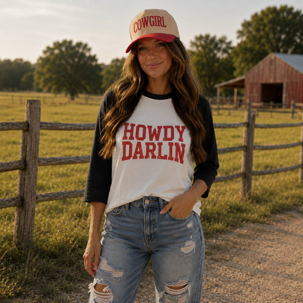 Southern cowgirl wearing Howdy Darlin raglan shirt and cowgirl hat on a rustic farm.