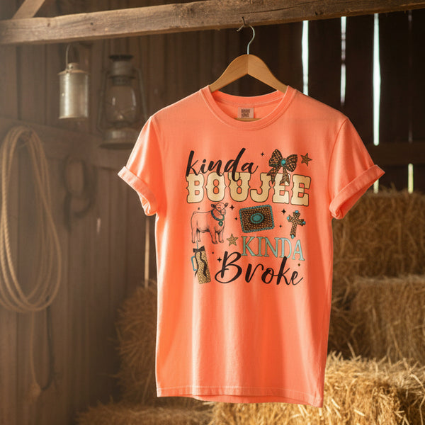 Kinda Boujee Kinda Broke steer show graphic t-shirt on neon cantaloupe Comfort Colors brand tee hanging in a barn